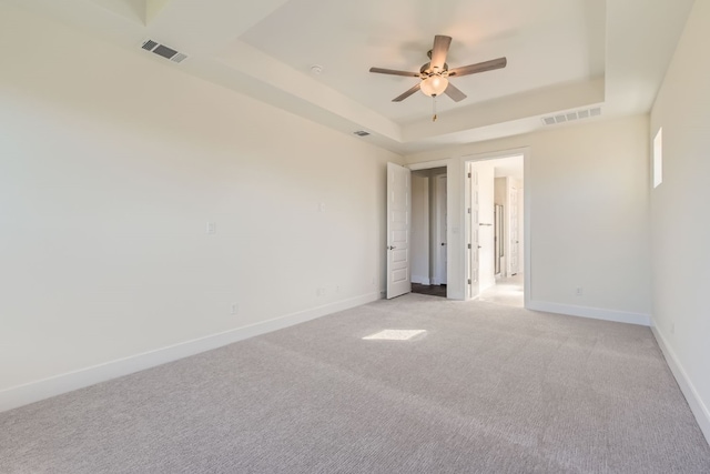 carpeted spare room with a raised ceiling and ceiling fan