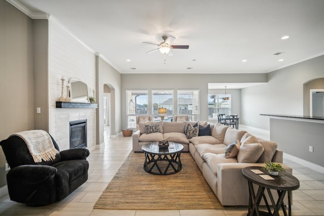 living room featuring a fireplace, light tile patterned flooring, ceiling fan, and crown molding