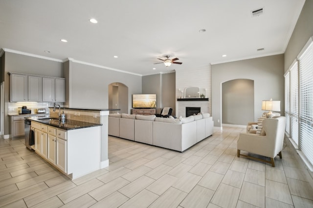 kitchen with white cabinetry, sink, a large fireplace, a kitchen island with sink, and dishwasher