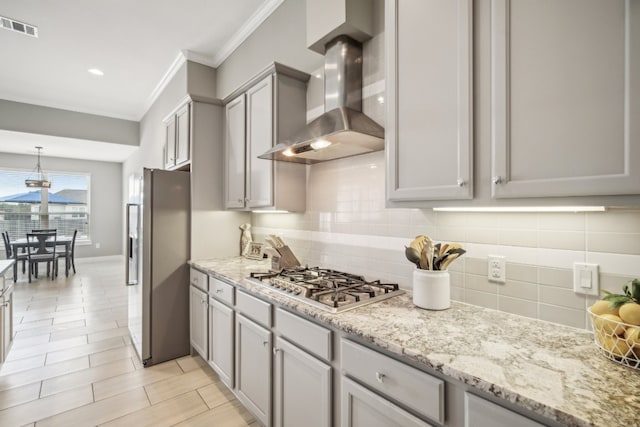 kitchen with stainless steel appliances, light stone counters, gray cabinets, wall chimney range hood, and decorative backsplash