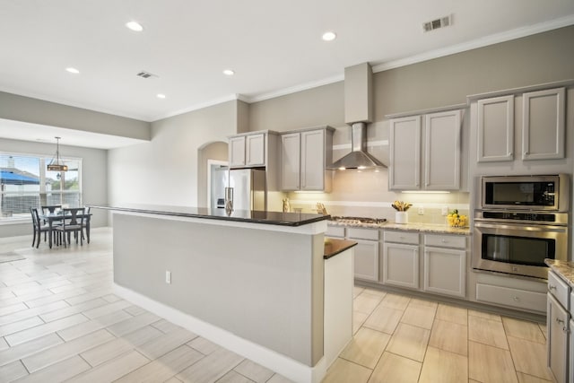 kitchen featuring wall chimney range hood, appliances with stainless steel finishes, gray cabinets, and a kitchen island