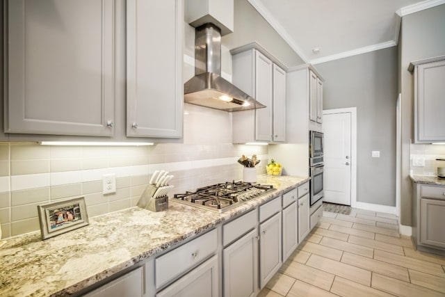 kitchen featuring crown molding, stainless steel appliances, wall chimney range hood, and gray cabinetry