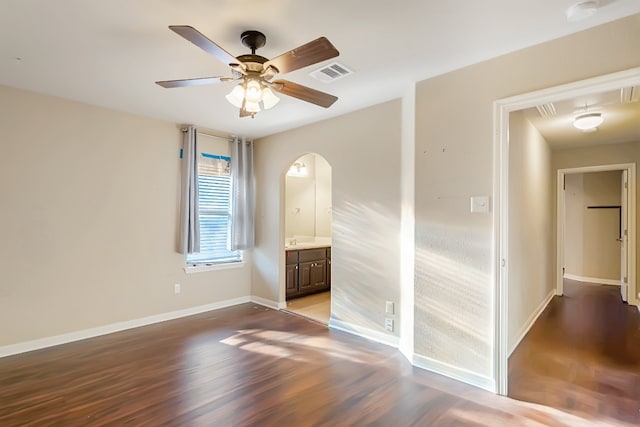 unfurnished bedroom with arched walkways, visible vents, ensuite bath, wood finished floors, and baseboards