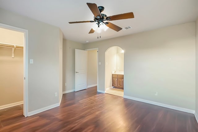 unfurnished bedroom with dark wood-style floors, baseboards, visible vents, and arched walkways