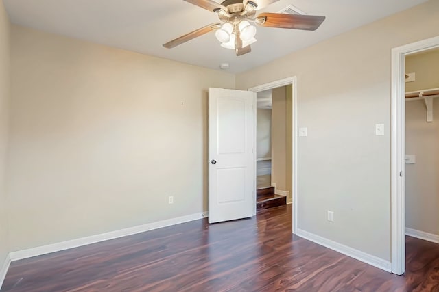 unfurnished bedroom with baseboards, dark wood finished floors, ceiling fan, a walk in closet, and a closet