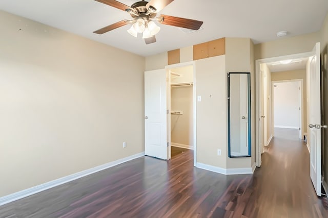 unfurnished bedroom featuring baseboards, ceiling fan, dark wood-type flooring, a walk in closet, and a closet