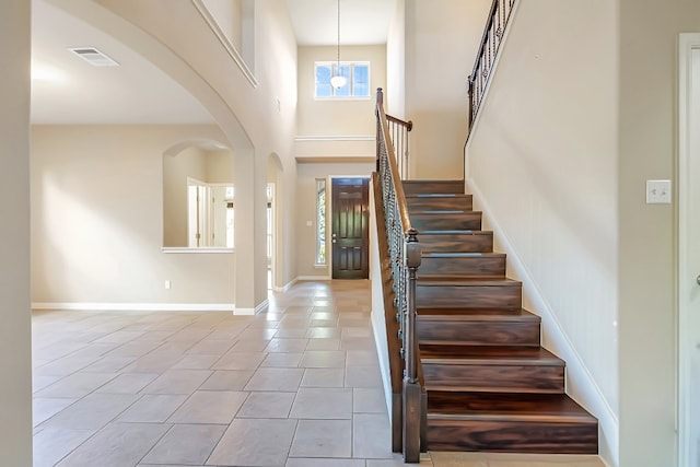 foyer entrance with light tile patterned floors, arched walkways, a towering ceiling, visible vents, and baseboards