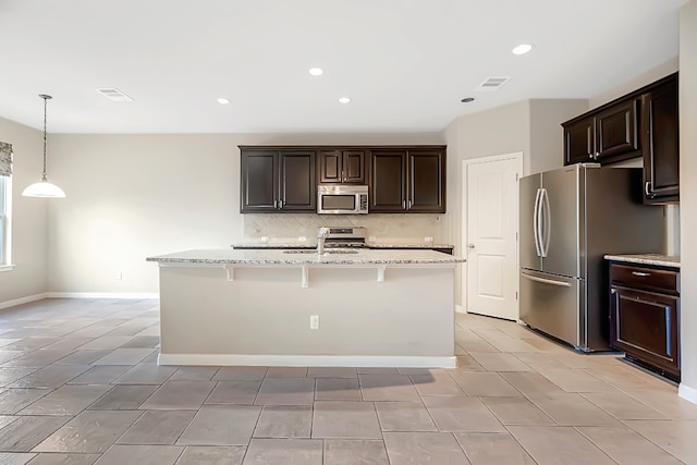 kitchen featuring light stone counters, appliances with stainless steel finishes, pendant lighting, sink, and a kitchen island with sink