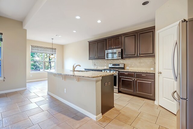 kitchen featuring dark brown cabinetry, a kitchen island with sink, stainless steel appliances, backsplash, and pendant lighting