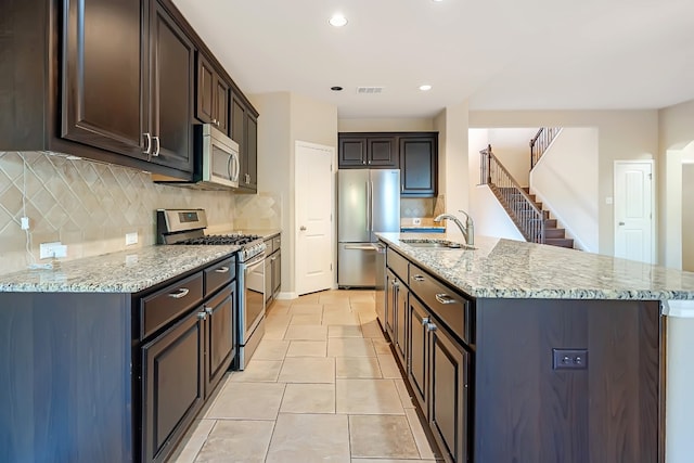 kitchen with light stone counters, stainless steel appliances, visible vents, a sink, and an island with sink