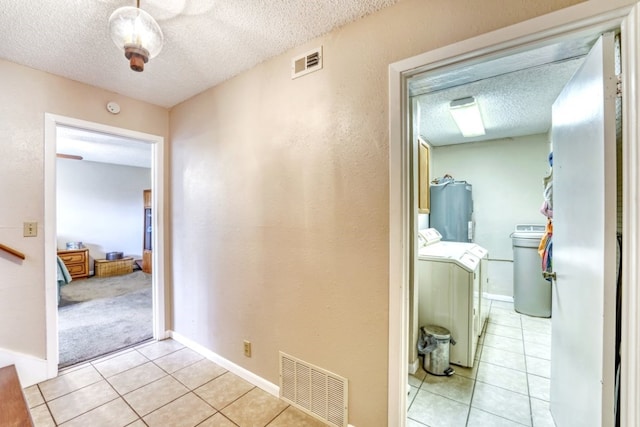 hallway featuring light tile patterned flooring, water heater, washing machine and dryer, and a textured ceiling