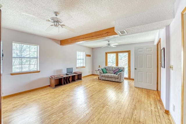 living room with ceiling fan, beamed ceiling, a textured ceiling, and light wood-type flooring