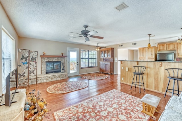 living room with ceiling fan, a tile fireplace, light hardwood / wood-style flooring, and a textured ceiling