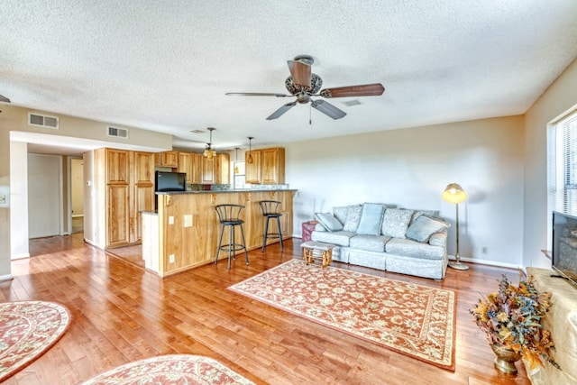 living room featuring ceiling fan, light hardwood / wood-style flooring, and a textured ceiling