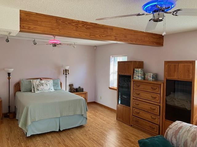 bedroom with ceiling fan, beam ceiling, a textured ceiling, and light wood-type flooring