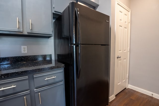 kitchen with dark stone counters, gray cabinets, black refrigerator, and dark hardwood / wood-style floors