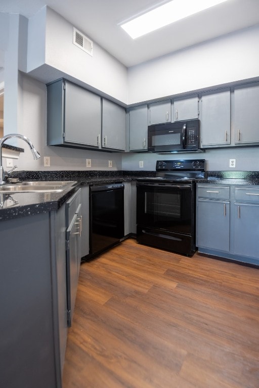 kitchen with black appliances, gray cabinetry, dark stone counters, dark hardwood / wood-style flooring, and sink