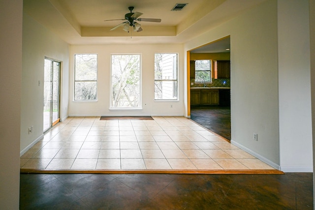 doorway featuring light tile patterned floors, a raised ceiling, visible vents, ceiling fan, and baseboards