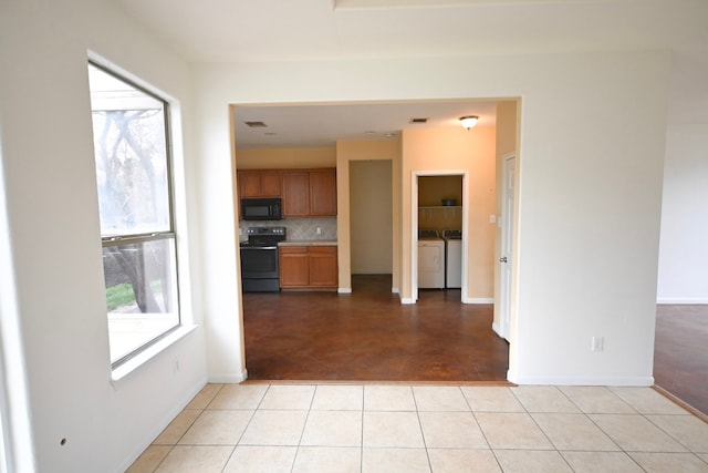 kitchen with a healthy amount of sunlight, black microwave, washing machine and dryer, and range with electric cooktop