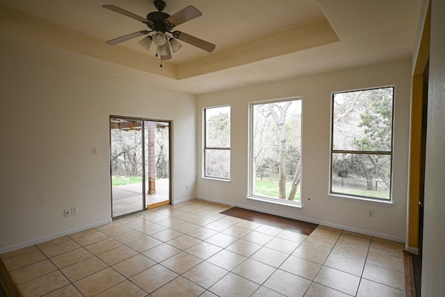 empty room featuring light tile patterned floors, baseboards, a tray ceiling, and a ceiling fan