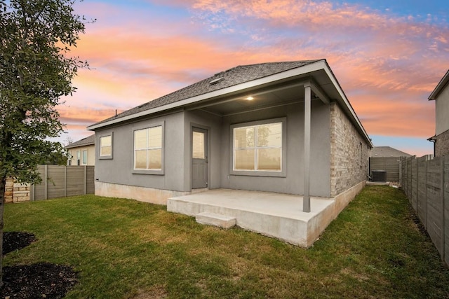 back house at dusk with a lawn, central AC unit, and a patio