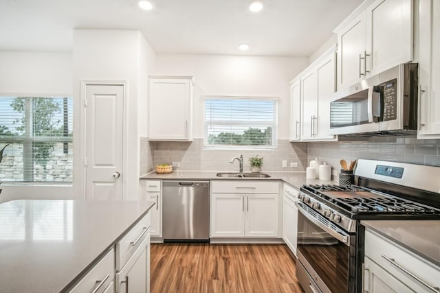 kitchen featuring sink, appliances with stainless steel finishes, decorative backsplash, white cabinets, and light wood-type flooring