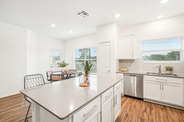 kitchen with sink, light hardwood / wood-style flooring, stainless steel dishwasher, a kitchen island, and white cabinetry