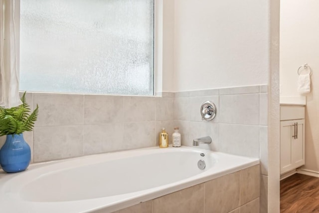 bathroom featuring hardwood / wood-style flooring, a relaxing tiled tub, and vanity