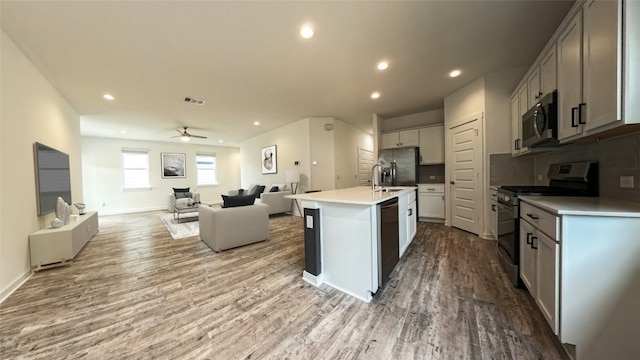 kitchen with a center island with sink, ceiling fan, light wood-type flooring, tasteful backsplash, and stainless steel appliances