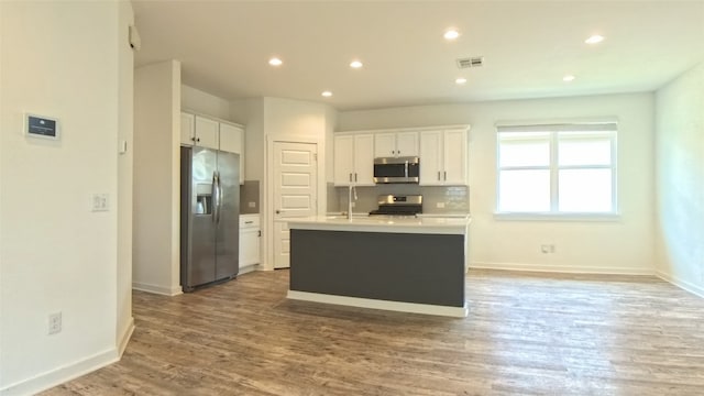 kitchen featuring hardwood / wood-style floors, backsplash, a kitchen island with sink, white cabinetry, and stainless steel appliances