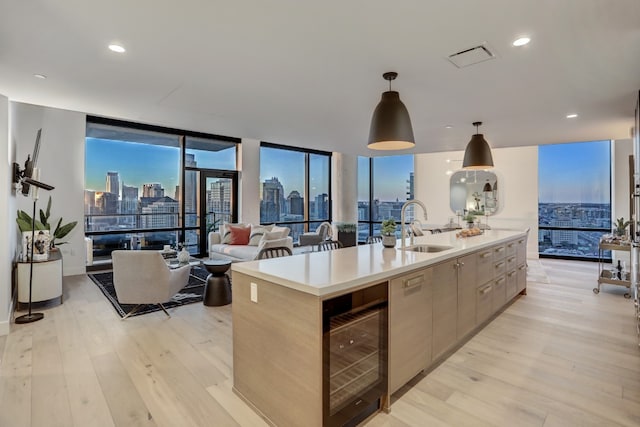 kitchen with floor to ceiling windows, a center island with sink, sink, hanging light fixtures, and beverage cooler