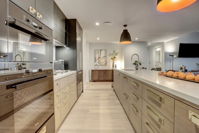 kitchen with pendant lighting, sink, radiator, light wood-type flooring, and stainless steel gas cooktop