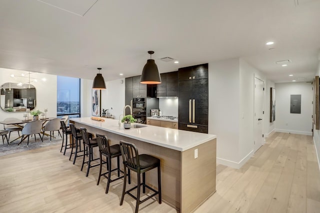 kitchen with decorative light fixtures, electric panel, a breakfast bar, light wood-type flooring, and an island with sink