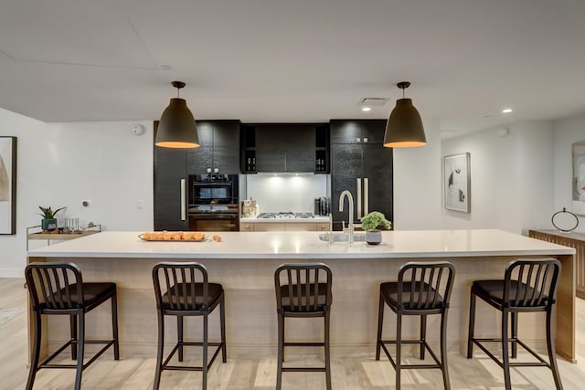 kitchen with hanging light fixtures, a kitchen island with sink, black appliances, and a breakfast bar area