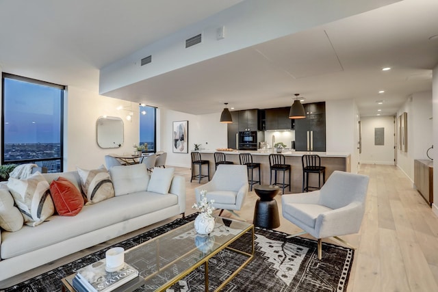 living room featuring floor to ceiling windows, electric panel, and light hardwood / wood-style flooring