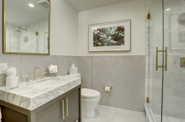 bathroom with tile patterned flooring, a shower with door, vanity, tile walls, and toilet