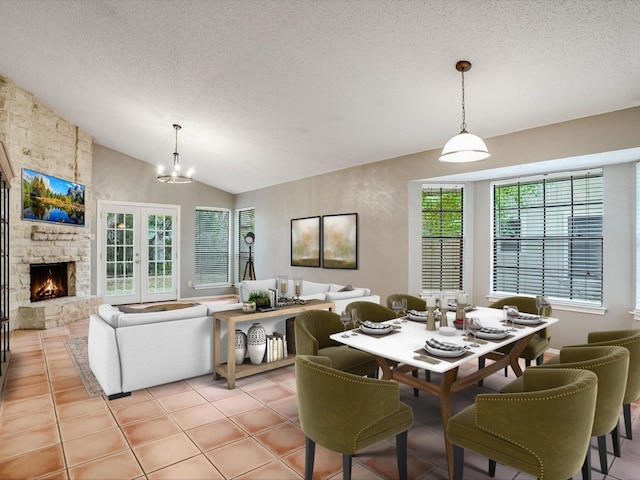 dining room with light tile patterned flooring, a textured ceiling, a stone fireplace, a chandelier, and lofted ceiling