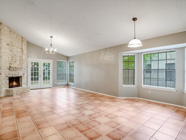 unfurnished living room with a textured ceiling, vaulted ceiling, a stone fireplace, a notable chandelier, and french doors