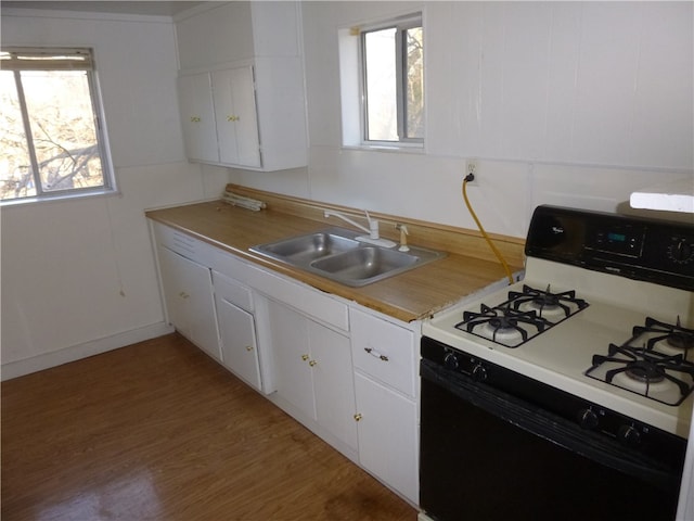 kitchen with gas range gas stove, wood-type flooring, white cabinets, and sink