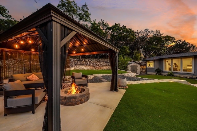 patio terrace at dusk featuring a gazebo, a shed, a yard, and an outdoor living space with a fire pit