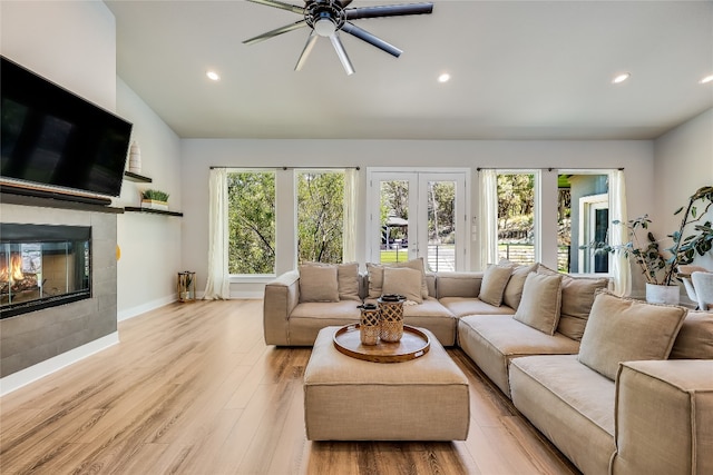 living room featuring light hardwood / wood-style floors, plenty of natural light, ceiling fan, and a tiled fireplace