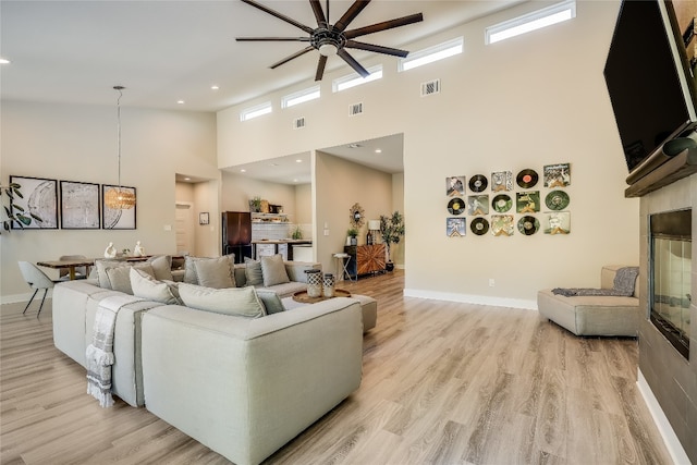 living room featuring ceiling fan, plenty of natural light, a towering ceiling, and light wood-type flooring