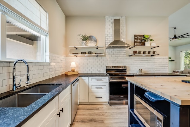 kitchen featuring wall chimney exhaust hood, stainless steel appliances, sink, white cabinets, and butcher block countertops