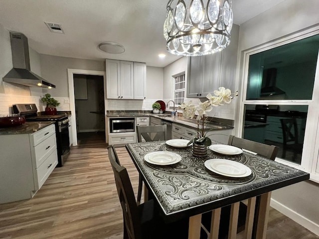 kitchen with stainless steel appliances, decorative backsplash, wall chimney range hood, white cabinetry, and decorative light fixtures