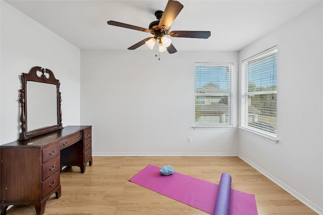 workout room with light wood-style flooring, a ceiling fan, and baseboards