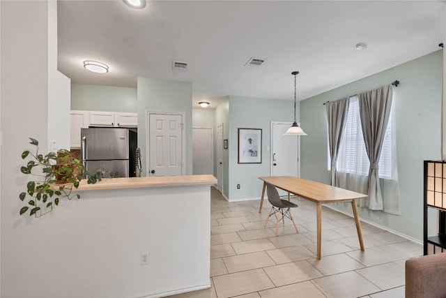 kitchen featuring visible vents, a peninsula, freestanding refrigerator, pendant lighting, and white cabinetry