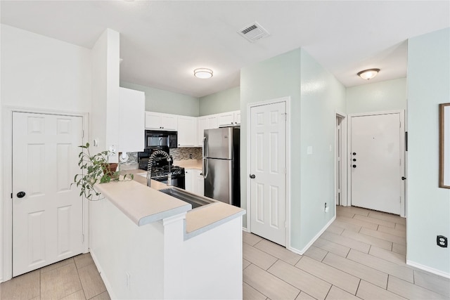 kitchen with visible vents, black appliances, a peninsula, white cabinets, and light countertops