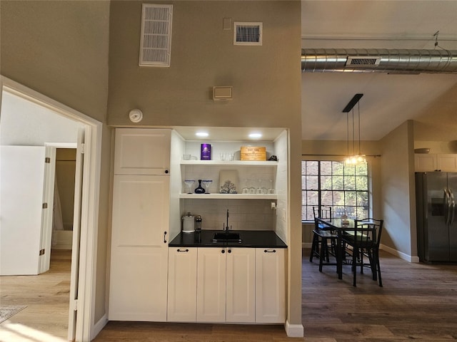 kitchen with pendant lighting, sink, stainless steel refrigerator with ice dispenser, white cabinetry, and wood-type flooring