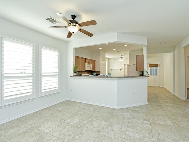 kitchen with light stone counters, kitchen peninsula, light tile patterned floors, ceiling fan, and white appliances