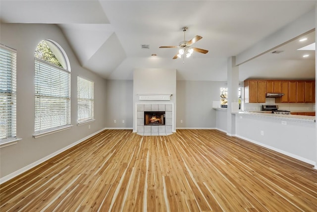 unfurnished living room featuring light wood-type flooring, ceiling fan, vaulted ceiling, a fireplace, and baseboards